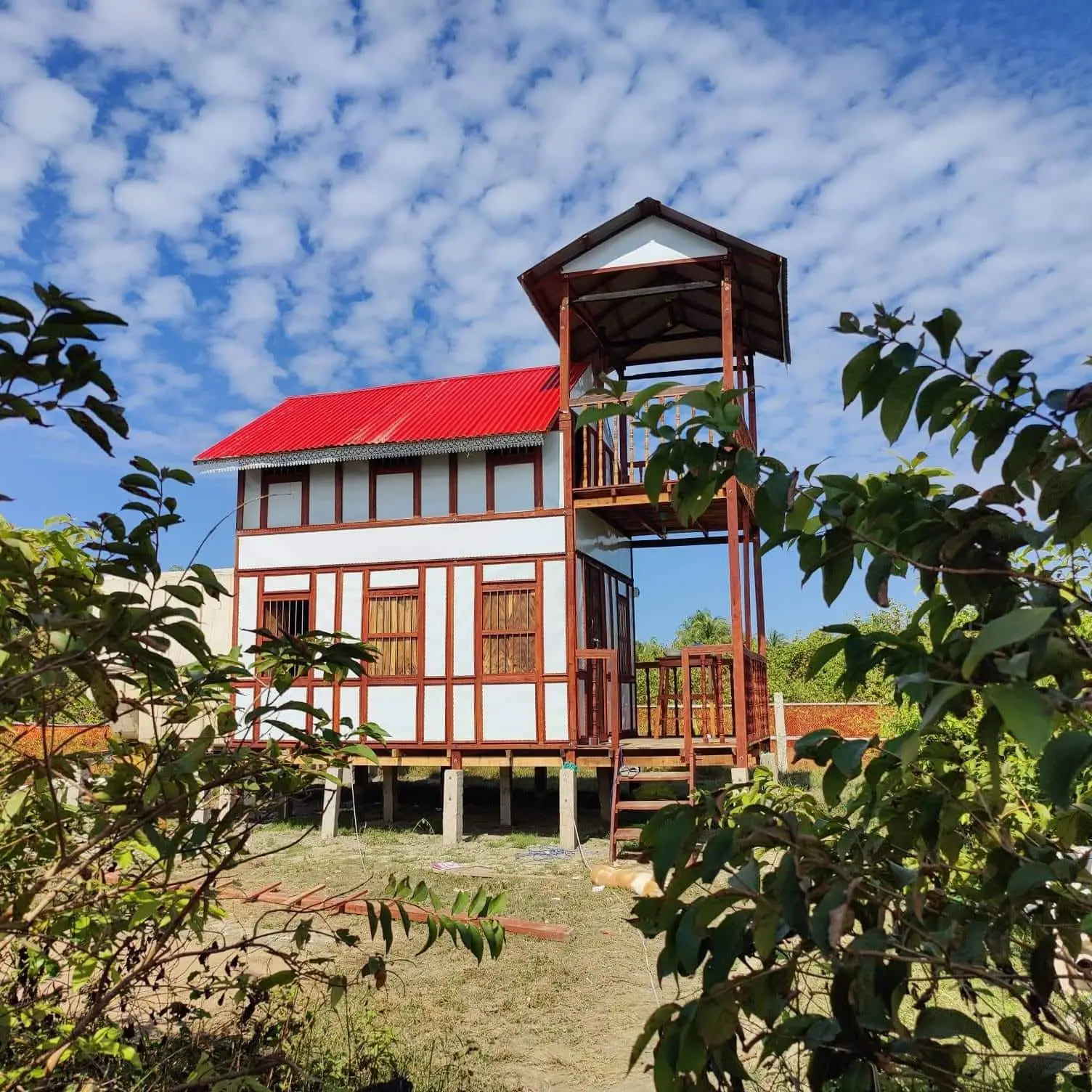Two-storey wooden cottage with a red roof and lookout tower under a sky of small clouds